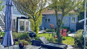 En uteplats med utemöbler, en grill och en trädgårdsdel med olika växter och ett träd.