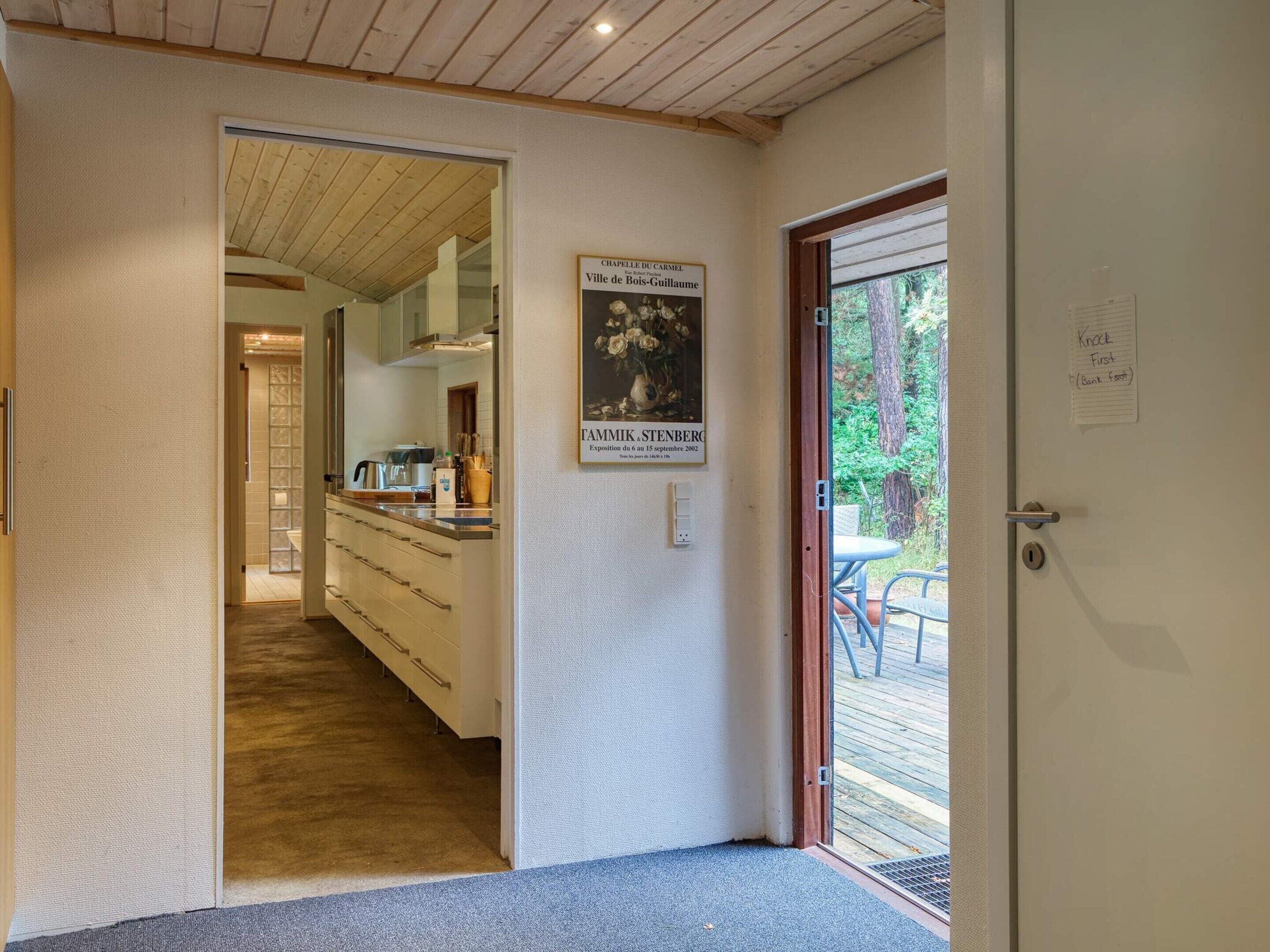 Un couloir mène à une cuisine dotée d’un plafond en bois, d’une œuvre d’art encadrée et d’une porte sur laquelle est apposée une pancarte indiquant : « Frapper avant d’entrer ».