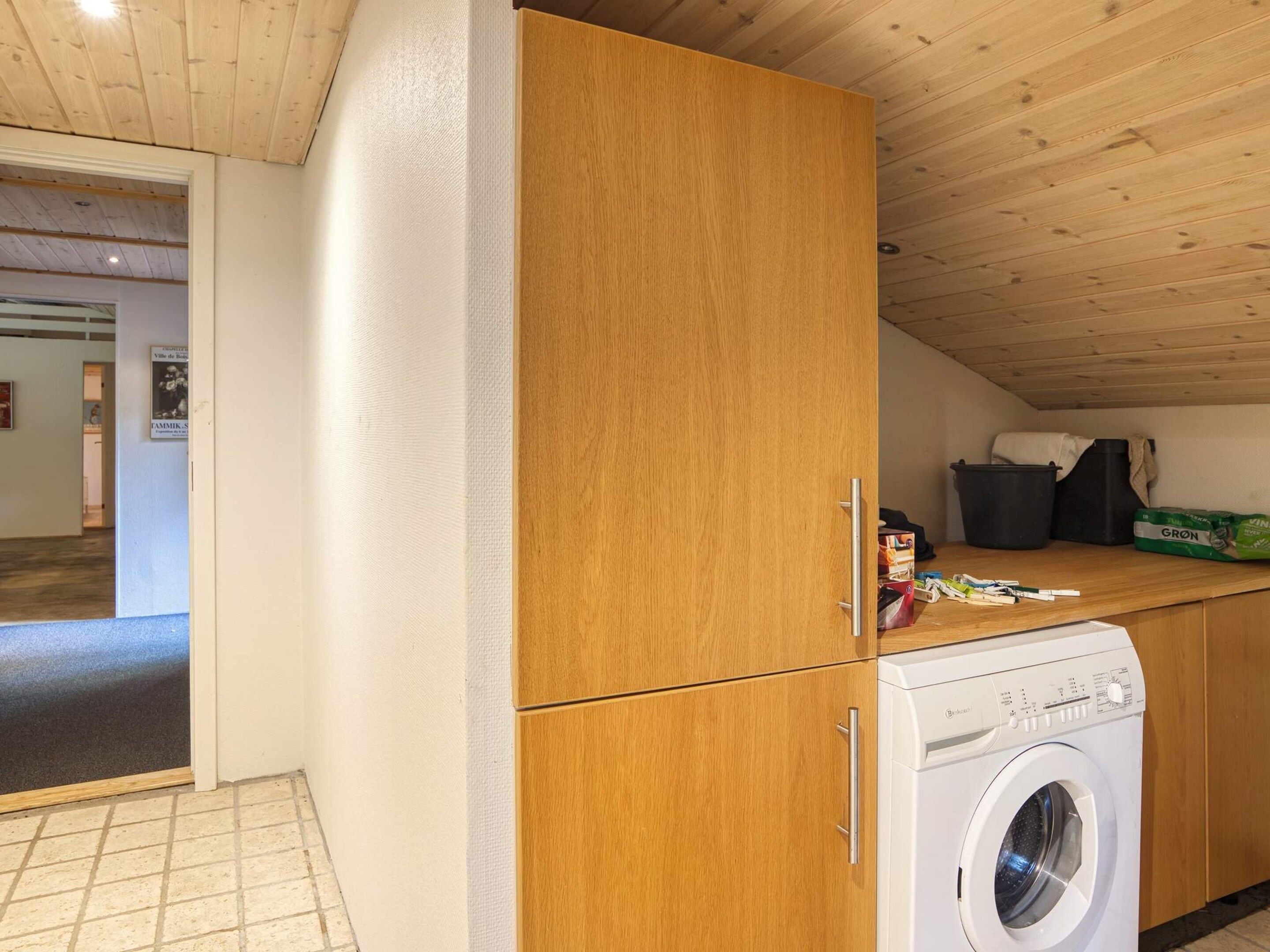 Une buanderie équipée d’un lave-linge, de meubles en bois et d’un sol carrelé.