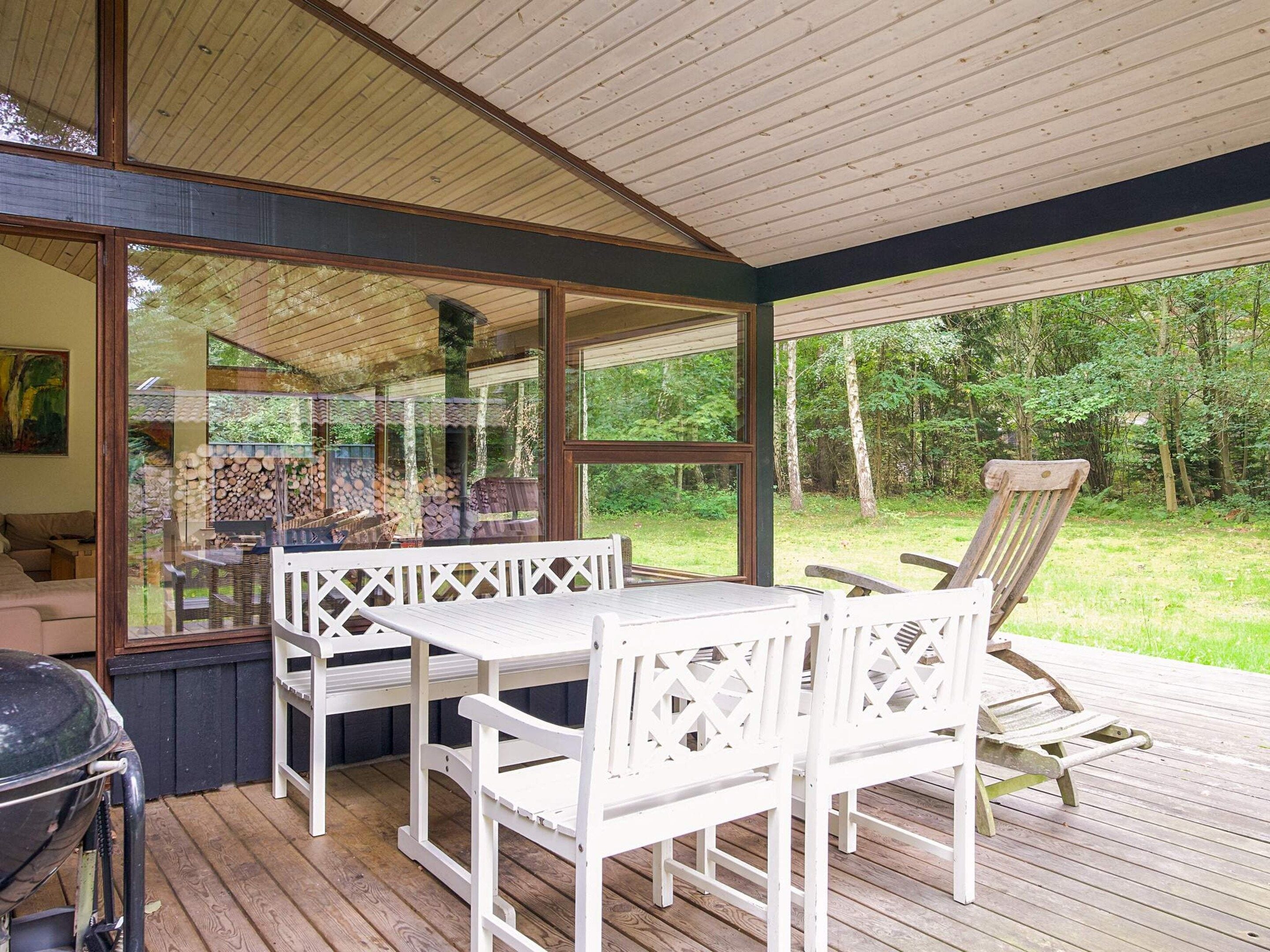 Um deck externo com mesa, cadeiras, churrasqueira e vista para uma área arborizada.