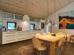 Een moderne keuken met witte kasten, een houten eettafel en een schilderij aan de muur.