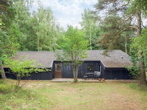 A rustic cabin with a tiled roof, a wooden door, and a small patio with outdoor furniture. - 4 Star Holiday Home in Farevejle (Faarevejle)