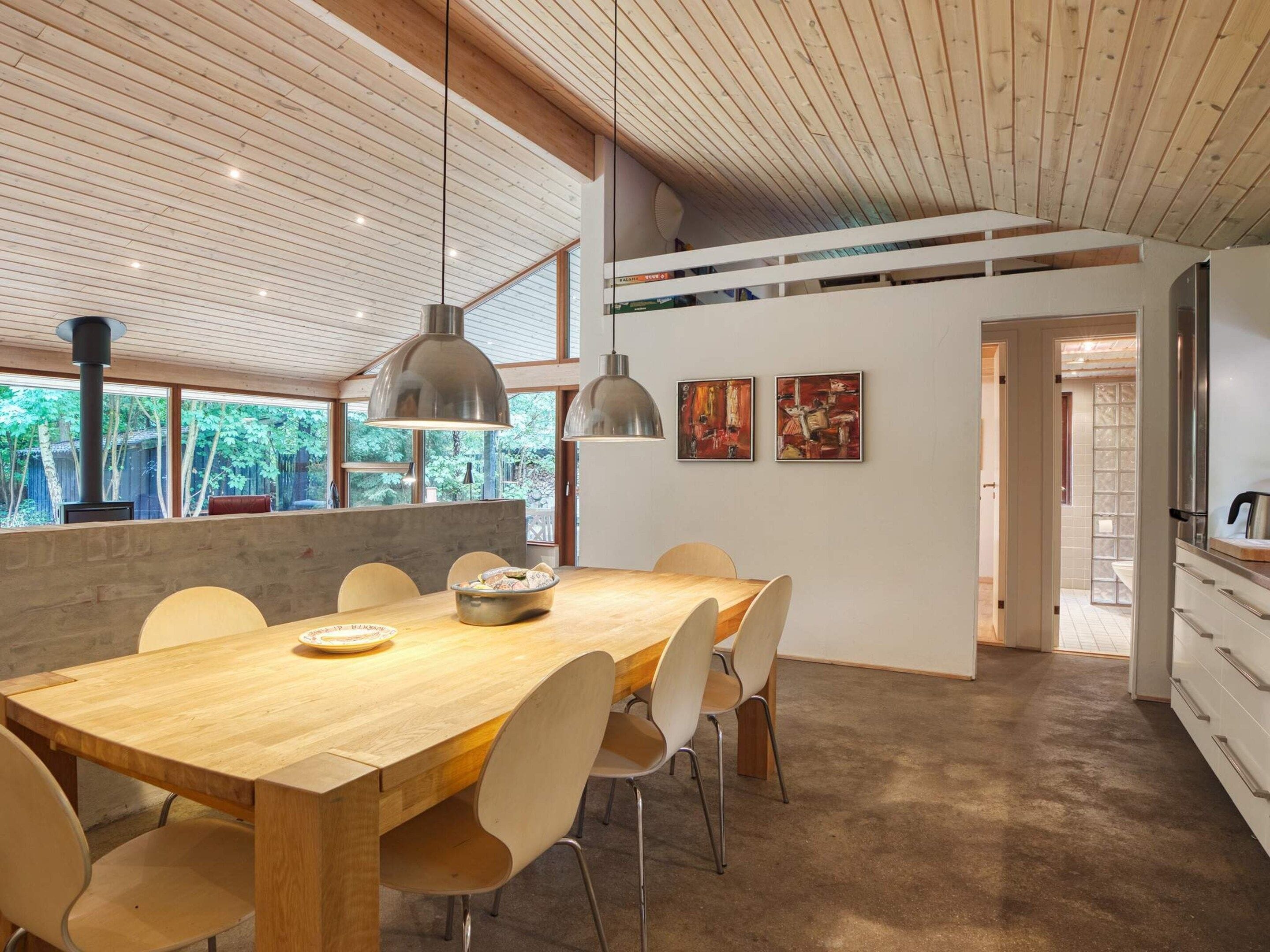 A modern dining area with a wooden table and chairs, pendant lighting, and artwork on the wall.