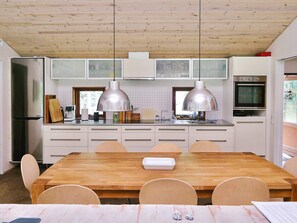 Une cuisine moderne avec des meubles en bois, un réfrigérateur en acier inoxydable, un four double et des luminaires suspendus.