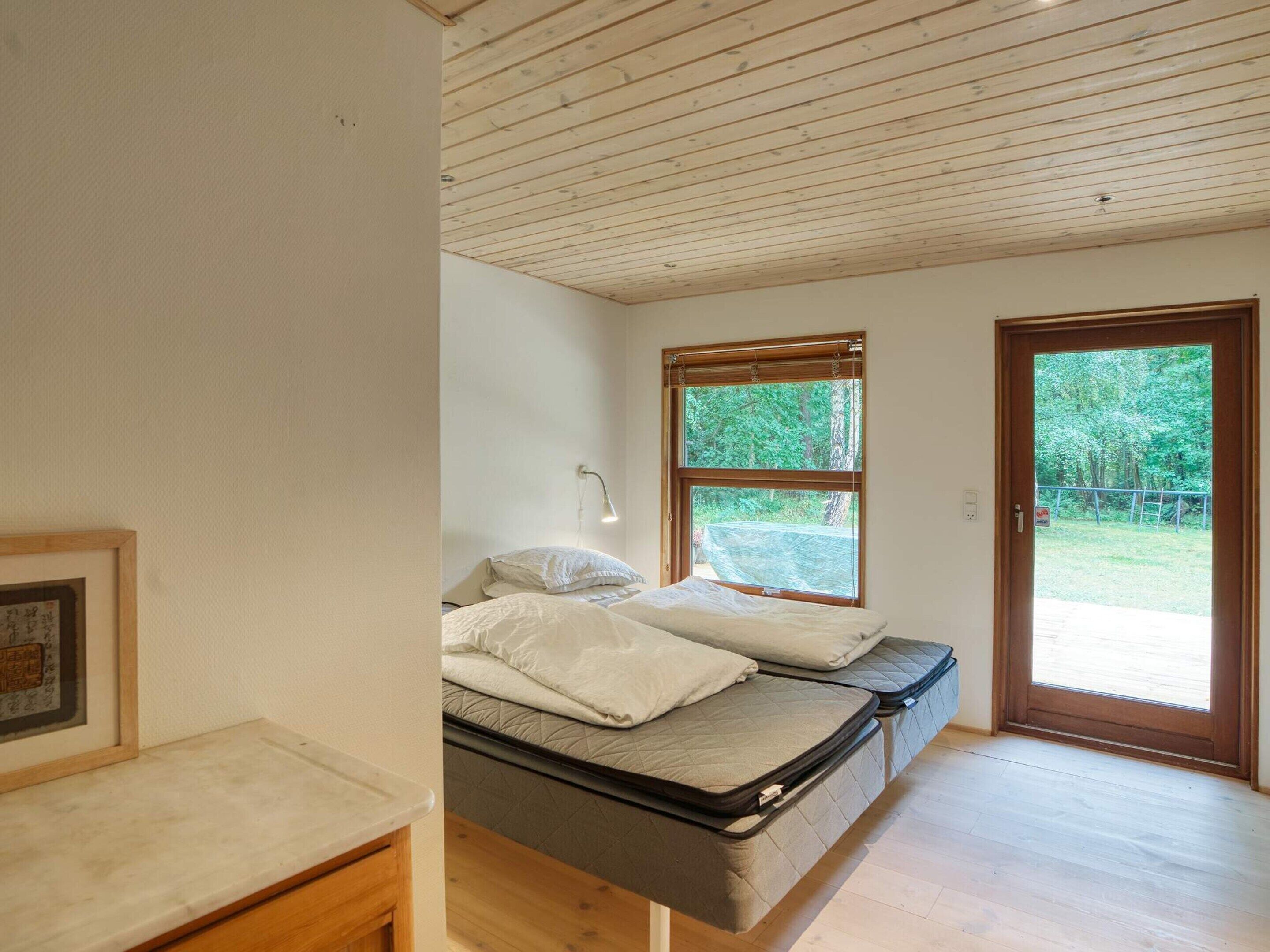 A bedroom with a bed, a bedside table, a window, and a door leading to an outdoor area.
