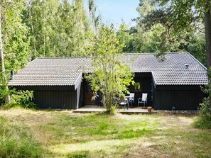 Een rustieke houten hut met pannendak, een klein terras met stoelen en een tuin.
