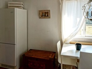 Ein gemütlicher Raum mit einem weißen Kühlschrank, einer Holzablage, einem weißen Tisch und einem Fenster mit Vorhängen.