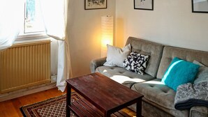 A living room with a sofa, a wooden coffee table, and a radiator. There are curtains on the window, and a lamp is on the wall. - 3 Person Holiday Home in Trosa (Trosa)