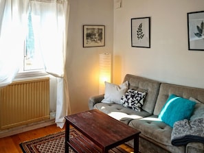 A living room with a sofa, a wooden coffee table, and a radiator. There are curtains on the window, and a lamp is on the wall. - 3 Person Holiday Home in Trosa (Trosa)
