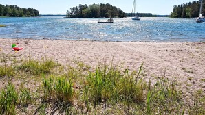 Une plage de sable avec des bateaux sur l’eau et une île boisée à l’horizon.