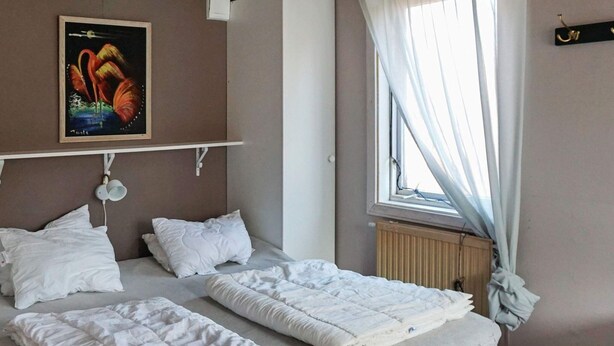 A bedroom with two beds, a radiator, a window with curtains, and a painting on the wall. - 3 Person Holiday Home in Trosa (Trosa)