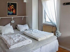 Ein Schlafzimmer mit zwei Betten, einem Heizkörper, einem Fenster mit Vorhängen und einem Bild an der Wand.