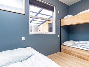 A room with a bunk bed, a single bed, a window with a view of an outdoor area, and a framed picture on the wall.