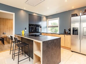 A modern kitchen with a central island, black bar stools, and a stainless steel refrigerator.