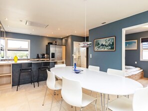 A modern kitchen with a built-in refrigerator, a dining area with a round table and chairs, and a painting on the wall. - 8 Person Holiday Home in Skagen (Skagen)
