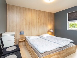 A bedroom with a wooden bed frame, a desk, a chair, and a window with a view of greenery. - 8 Person Holiday Home in Skagen (Skagen)