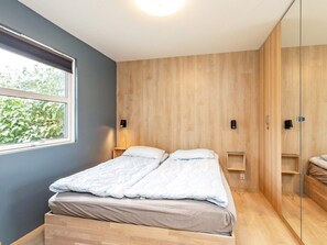 A bedroom with a bed, bedside tables, a wardrobe, and a window with a view of greenery. - 8 Person Holiday Home in Skagen (Skagen)
