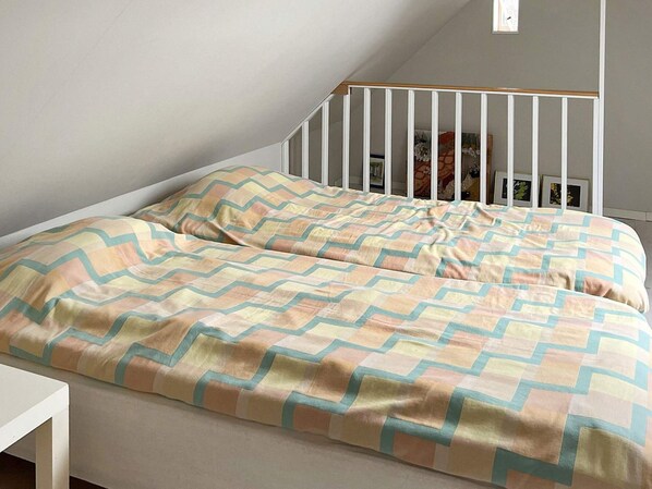 A bedroom with a bed, a white railing, and a window.