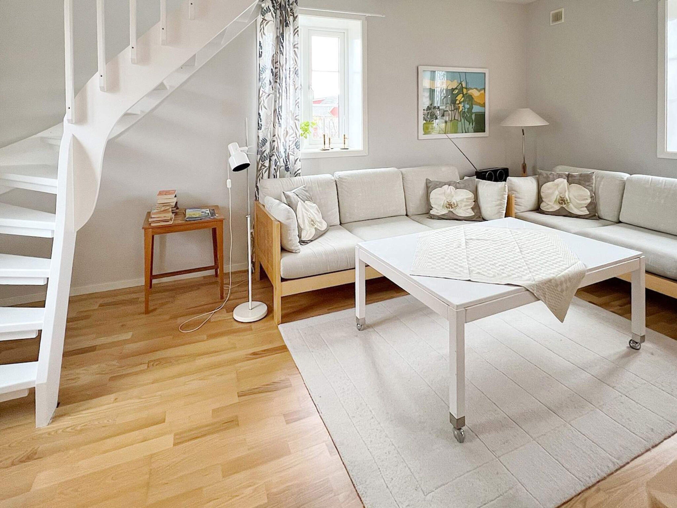 A modern living room with a white sofa, a coffee table, a floor lamp, and a staircase.