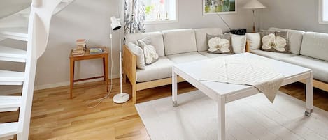 A modern living room with a white sofa, a coffee table, a floor lamp, and a staircase.