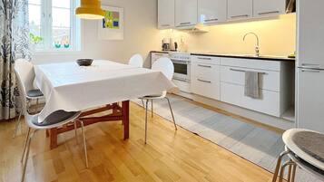 A modern kitchen with white cabinets, a dining table with chairs, and a window with curtains.