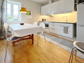 A modern kitchen with white cabinets, a dining table with chairs, and a window with curtains.