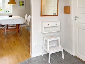 Ett rum med ett vitt bord och stolar, en liten vit hylla, en spegel och en dörr.