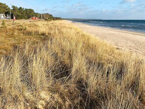 A beach with sand, grass, and a distant red building. - 4 Person Holiday Home in Yngsjo, Sverige (Yngsjo)