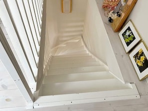 Un escalier avec des rampes et des marches blanches, menant à un palier doté d’une structure en bois et agrémenté d’un arrangement floral.