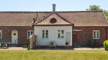 A two-story building with a tiled roof, a front porch, and a small garden area.
