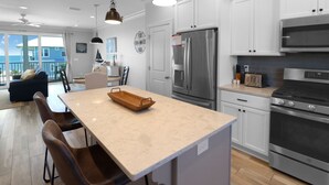 Une cuisine moderne dotée d’un îlot central, d’appareils électroménagers en acier inoxydable et offrant une vue sur l’extérieur.