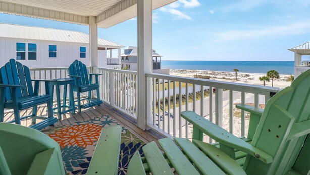 Une véranda abritée, avec des fauteuils Adirondack verts, un tapis à motifs et une vue sur la plage et l’océan.