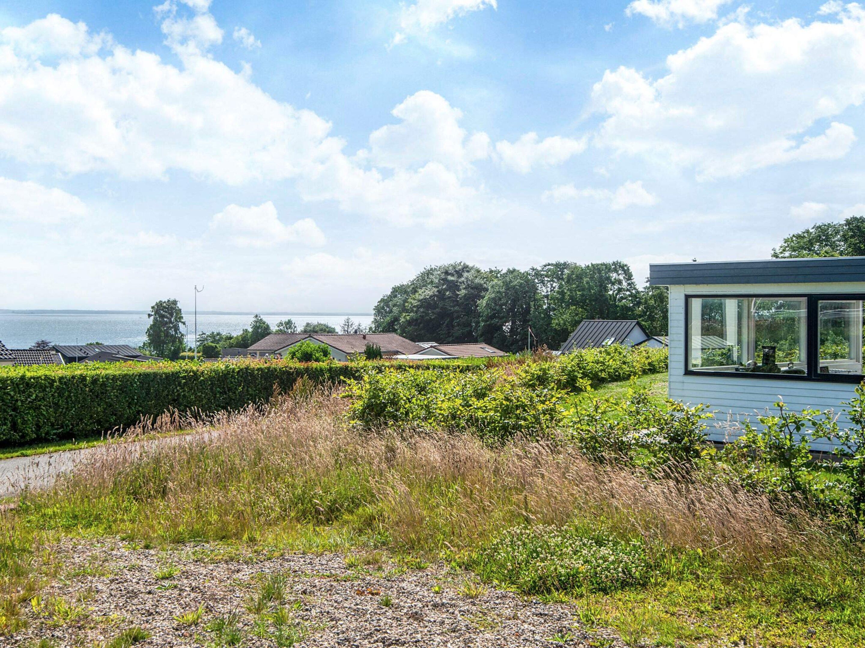 A modern house with a large glass window, surrounded by a well-maintained garden and a view of the sea.