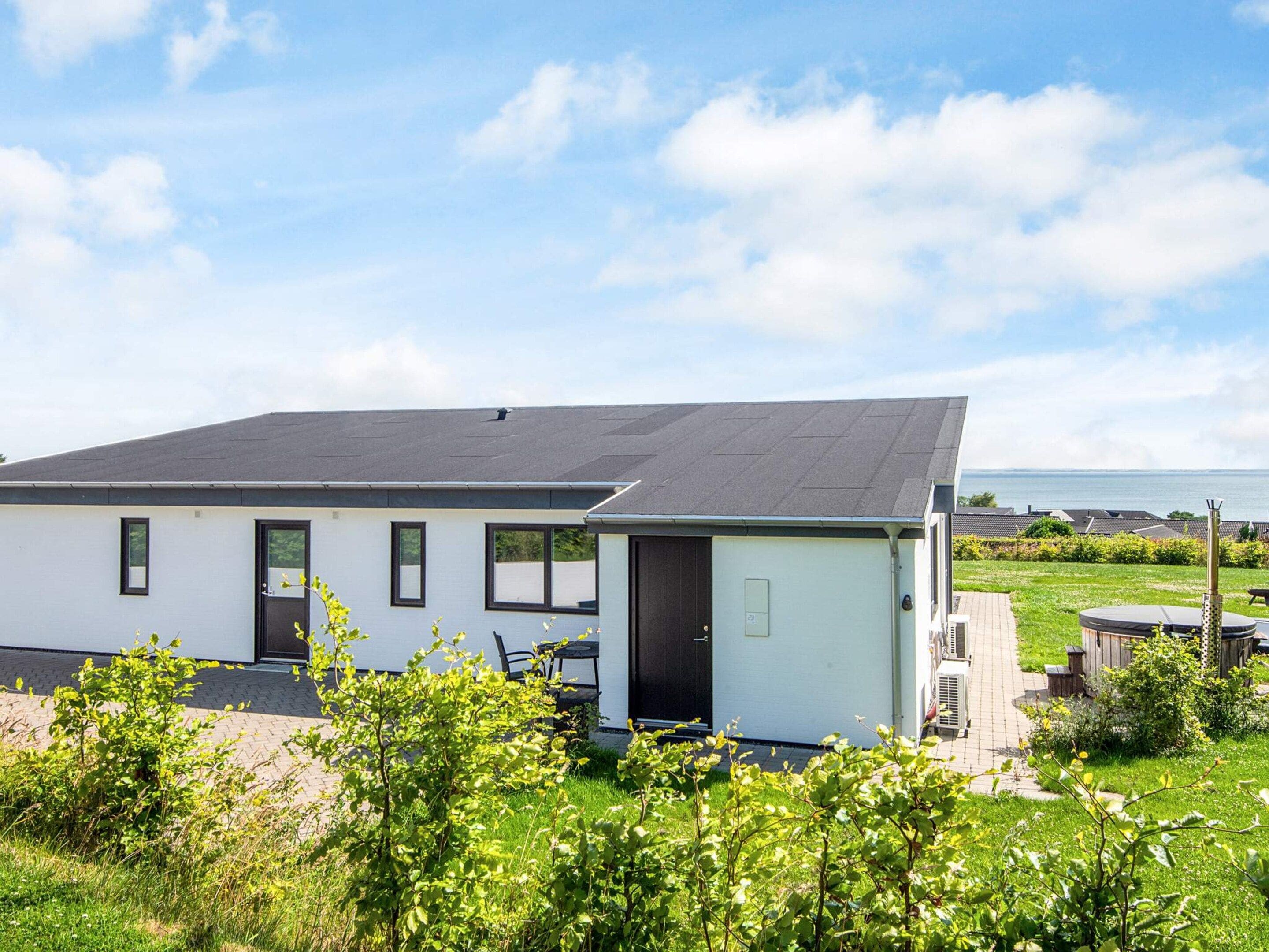 A modern two-story house with a flat roof, large windows, and a view of the sea.