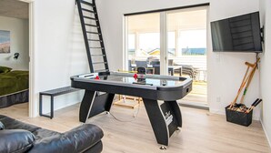 A modern living room with a foosball table, a sofa, a TV, and a balcony with a view. - 10 Person Holiday Home in Sjolund (Sjølund)