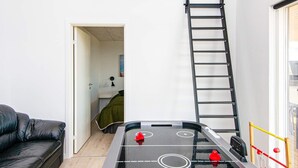 A room with a foosball table, a black leather sofa, a ladder, and a door leading to another room. - 10 Person Holiday Home in Sjolund (Sjølund)