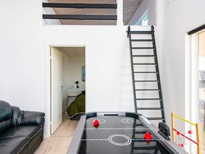 Ein Zimmer mit einem Tischkicker, einer schwarzen Ledersofa, einer Leiter und einer Tür zu einem weiteren Raum.