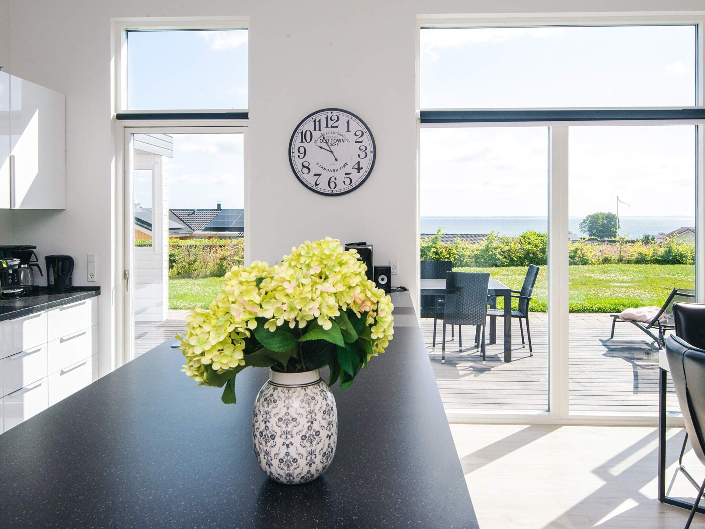 Une cuisine moderne avec une grande fenêtre, une horloge et un vase de fleurs.