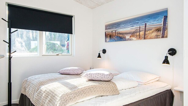 A bedroom with a bed, a window with a view, a painting on the wall, and two wall-mounted lamps. - 10 Person Holiday Home in Sjolund (Sjølund)
