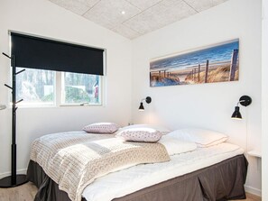 A bedroom with a bed, a window with a view, a painting on the wall, and two wall-mounted lamps.