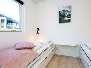 Ein Schlafzimmer mit einem Bett, einem Nachttisch, einer Wandlampe, einem Fenster und einem gerahmten Bild an der Wand.