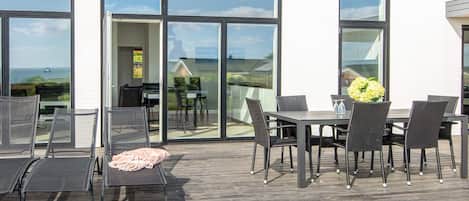 An outdoor patio with a table and chairs, a wooden deck, and large glass doors leading to an interior space.