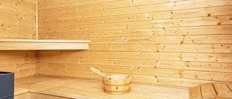 A sauna room with wooden walls, a bench, and a wooden bucket.
