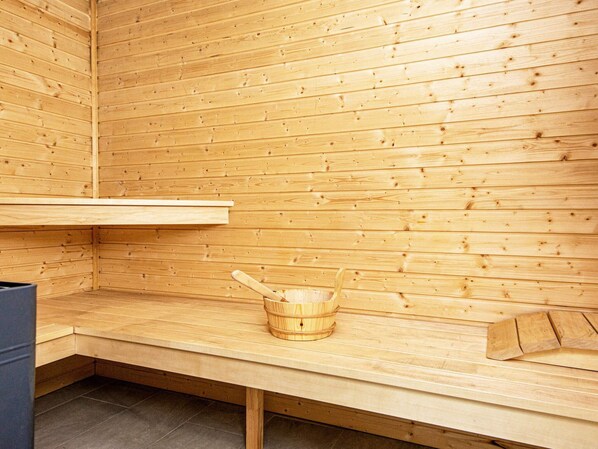 A sauna room with wooden walls, a bench, and a wooden bucket.