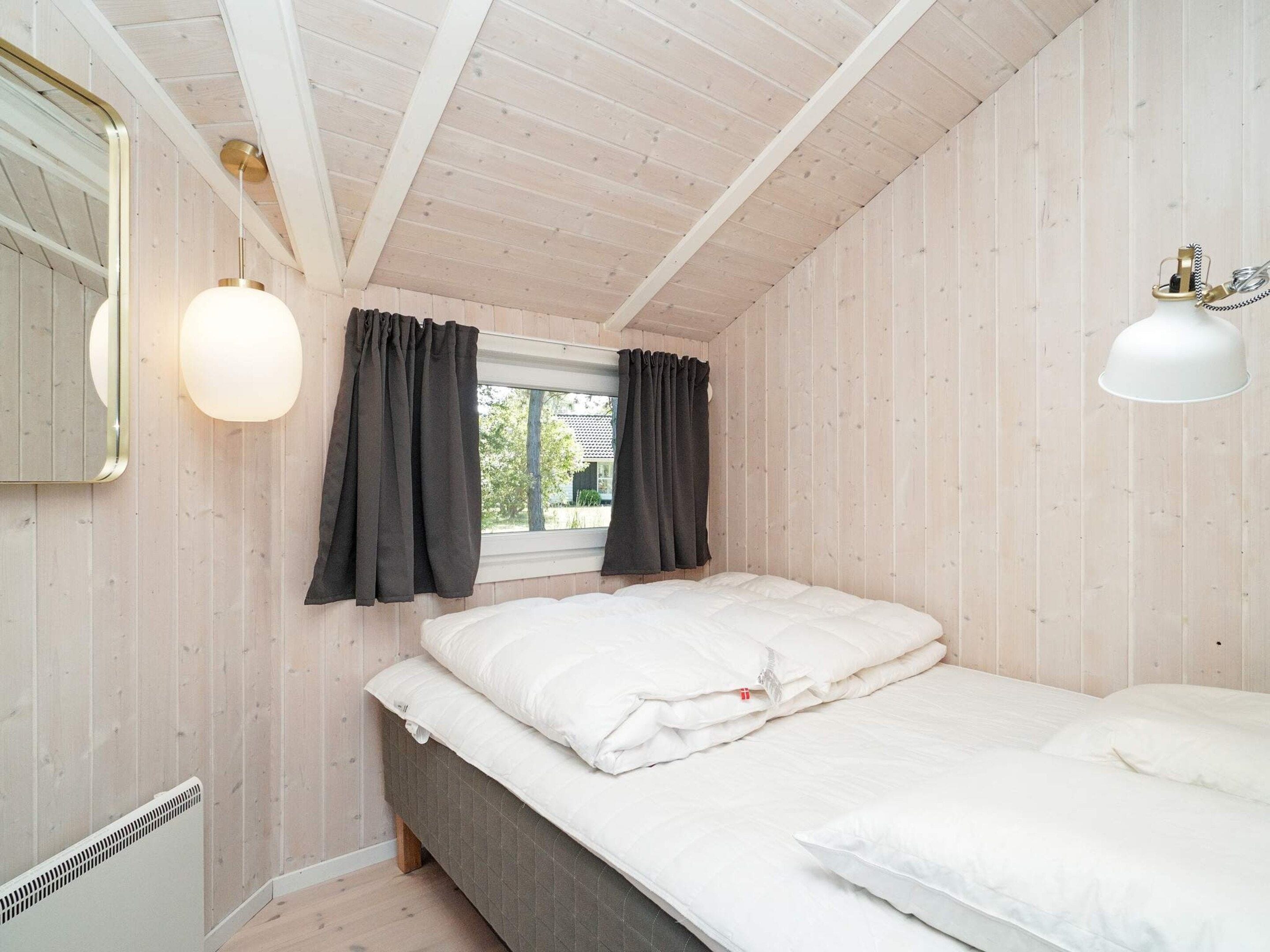 Un dormitorio con cama, ventana con cortinas, radiador y lámpara colgante.