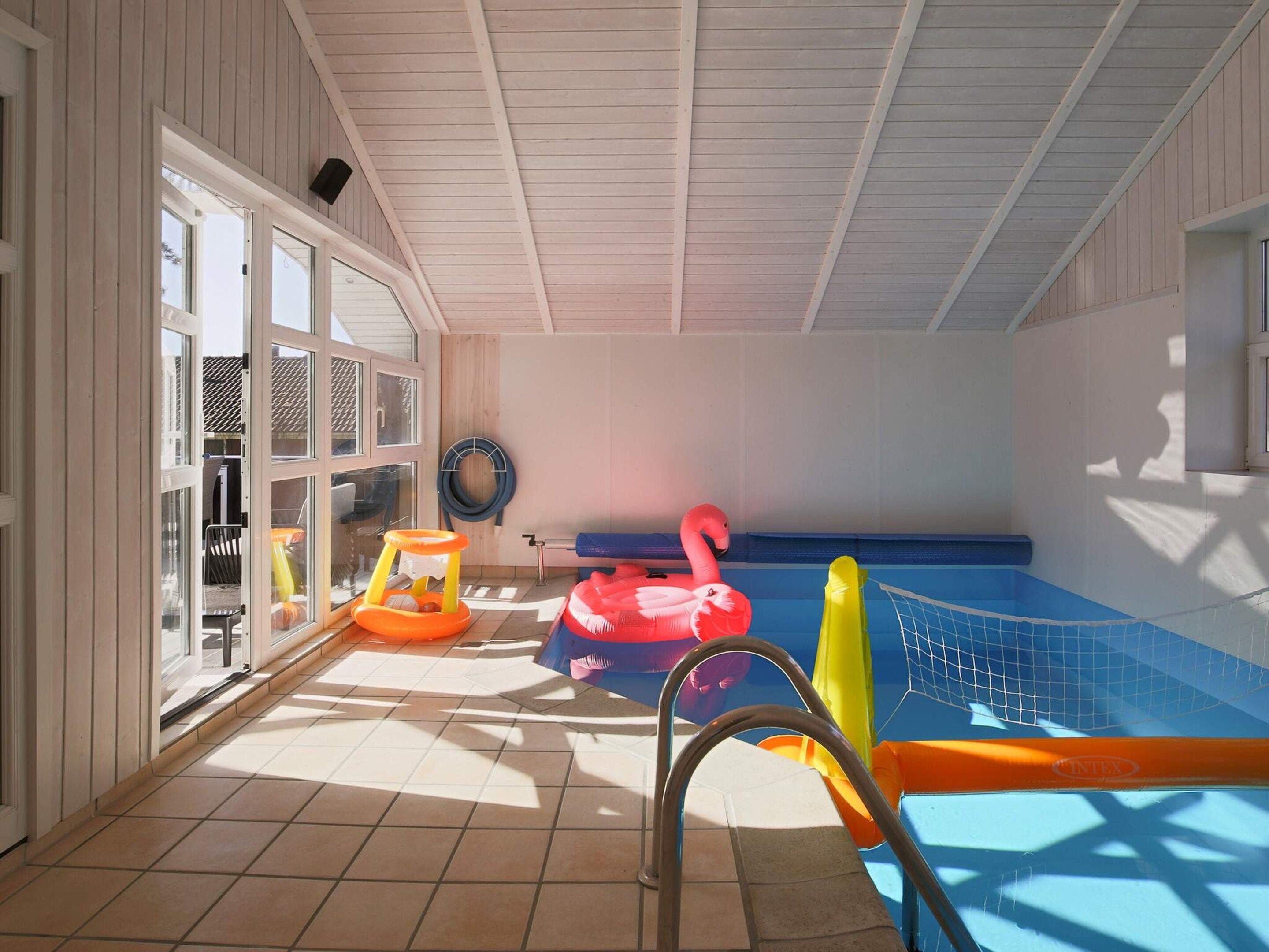 Una piscina interior con suelo de baldosas, una escalera de piscina y juguetes inflables.