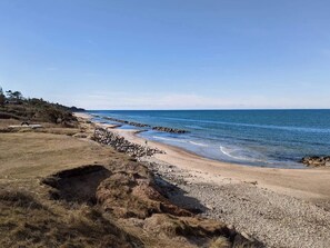 Un paisaje costero con una playa arenosa, una costa rocosa y un cielo despejado.