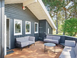 A covered outdoor seating area with a dark wooden exterior, white trim, and a view of trees and greenery. - 7 Person Holiday Home in Graested (Gilleleje)