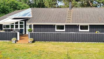 Et hus med mørk facade, tagtækket med fliser, og en overdækket veranda.