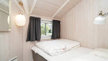 Un dormitorio con cama, ventana con cortinas, radiador y lámpara fijada a la pared.